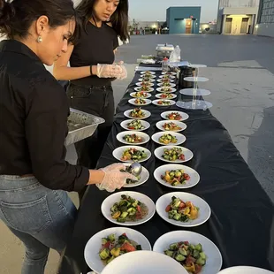 two women serving food on a long table
