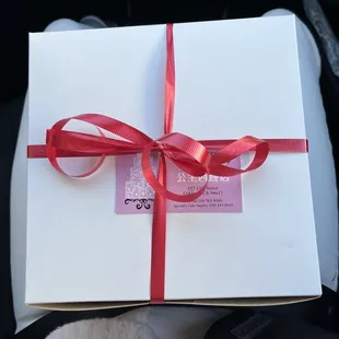 a gift wrapped in white paper with a red ribbon