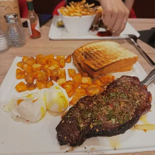 Steak and eggs with cut potatoes and a side of toasted white bread