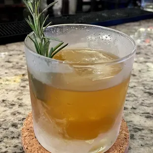 a drink in a glass with a sprig of rosemary
