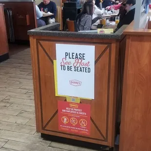 a restaurant counter with a sign that reads please to be seated