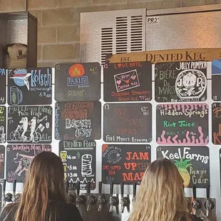 two women standing in front of a wall of beer