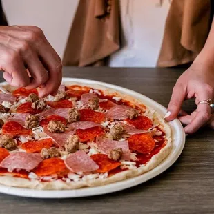 a person putting toppings on a pizza