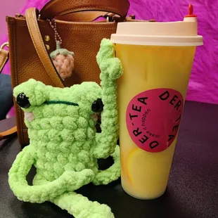 a crocheted frog next to a cup of coffee