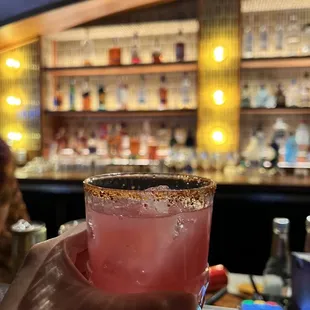 a person holding a drink in front of a bar