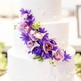 a white wedding cake with purple flowers