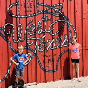 two children standing in front of a mural