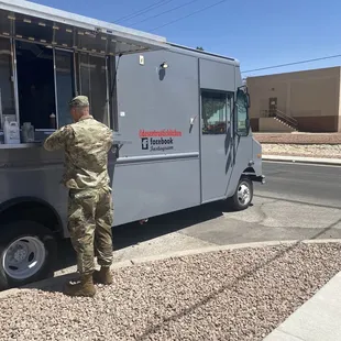 a man in camouflage standing in front of a food truck