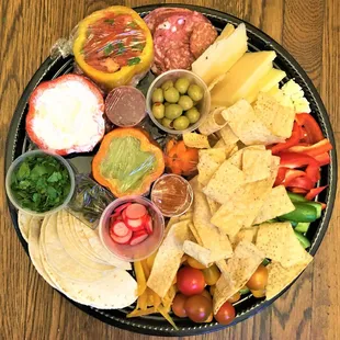 a platter of food including tortillas, chips, salsa, tomatoes, peppers, olives, tomatoes, and