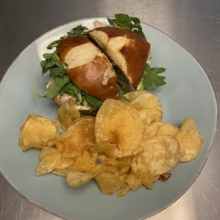 Turkey, Brie, apple, arugula, and fig jam sandwich on pretzel bun with chips.