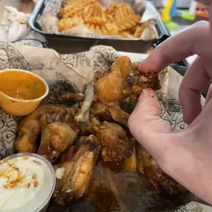a hand grabbing a piece of chicken wings