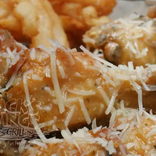 a closeup of chicken wings and fries with grated parmesan cheese
