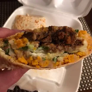 a hand holding a taco in a styrofoam container