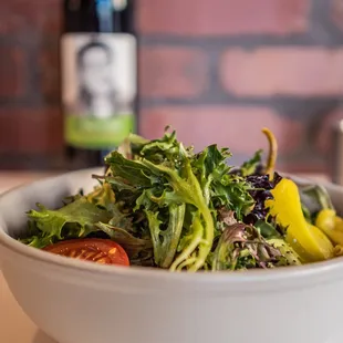 a bowl of salad with a bottle of wine in the background