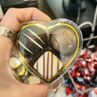 a hand holding a heart shaped box of chocolates