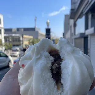 a hand holding a bun with a bite taken out of it