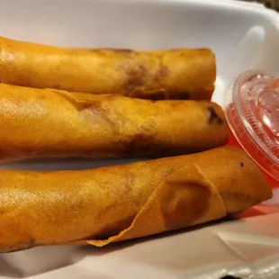 three fried spring rolls in a styrofoam container
