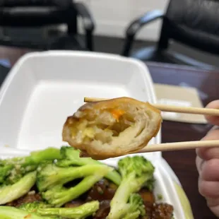 a person holding chopsticks over a dish of broccoli