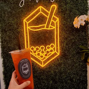 a person holding a drink in front of a neon sign