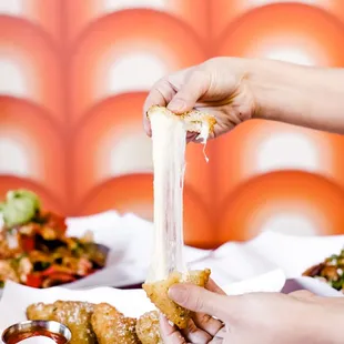 a person holding a piece of cheese over a plate of food