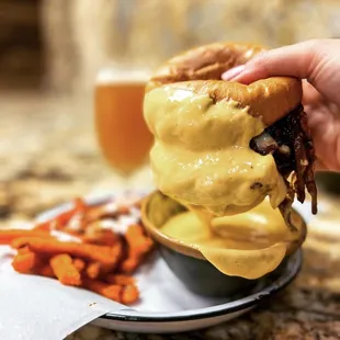a hand holding a sandwich over a bowl of fries