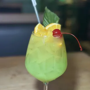 a green cocktail with a cherry garnish