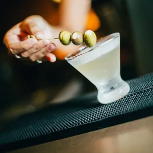 a person holding a martini glass with olives