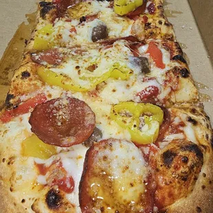 Mad pizza with pepperoni banana peppers olives and arugala