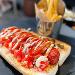 Classic Street (Dirty) Dog: All beef hotdog wrapped in bacon, aioli, grilled peppers, onions, pico de gallo, ketchup, fries | $11