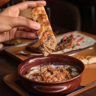 a person dipping a piece of bread into a bowl of soup