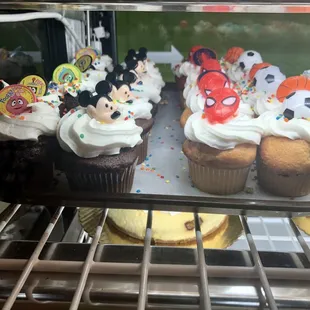 Dark and light brown muffins with white frosting, decorated with animated and superhero movie character faces.