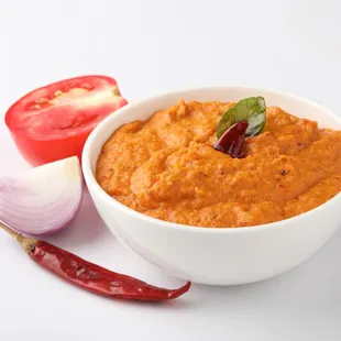 a bowl of dip with a tomato and onion on the side