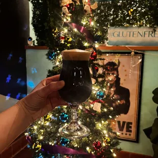 a person holding a glass of beer in front of a christmas tree