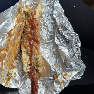 a hot dog wrapped in foil with ketchup and mustard