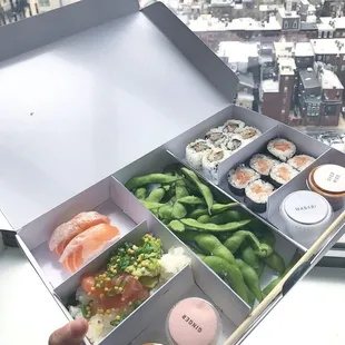 a person holding a box of sushi