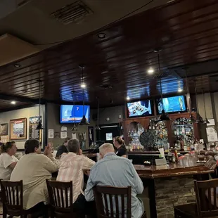 people sitting at a bar watching tvs