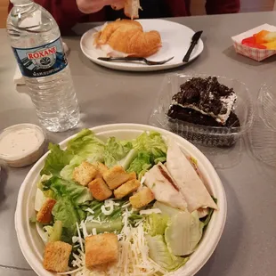 Caesar salad, turkey croissant sandwich with fruit, and an oreo brownie.