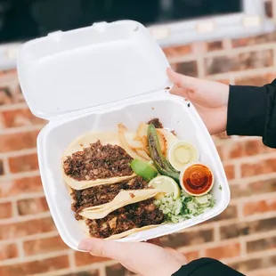 a person holding a container of tacos