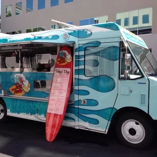 a blue food truck with a surfboard sticking out of the side