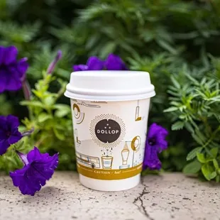 a cup of coffee on a table surrounded by purple flowers