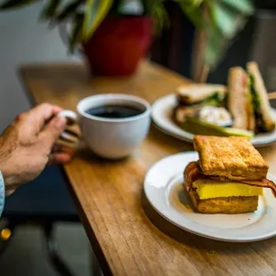 a person holding a cup of coffee and a sandwich