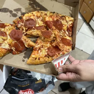 a hand holding a box of pepperoni pizza