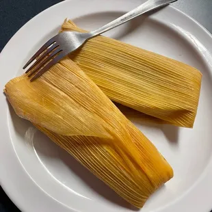 two tamales on a plate with a fork