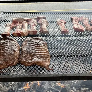 steaks and ribs cooking on a grill