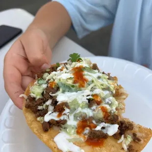Taco vampiros (description: tostada with melted mozzarella, asada, cabbage, cilantro, crema, guacamole salsa, red and green salsa)