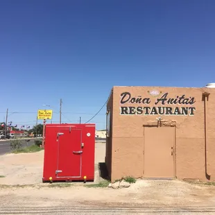 a red refrigerator in front of a tan building