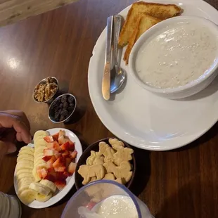 Oatmeal with toast, side fruit such as banana slices, strawberries, animal cookies, pecans, raisins.