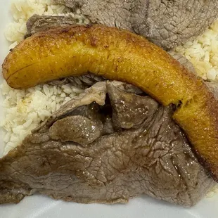 a plate of meat and rice with a banana