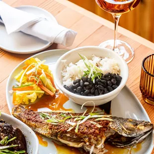 a plate of fish, rice, beans, and a glass of wine