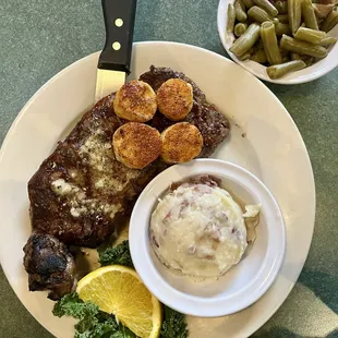 Ribeye steak with seared scallops, mashed red potatoes, and green beans cooked with bacon
